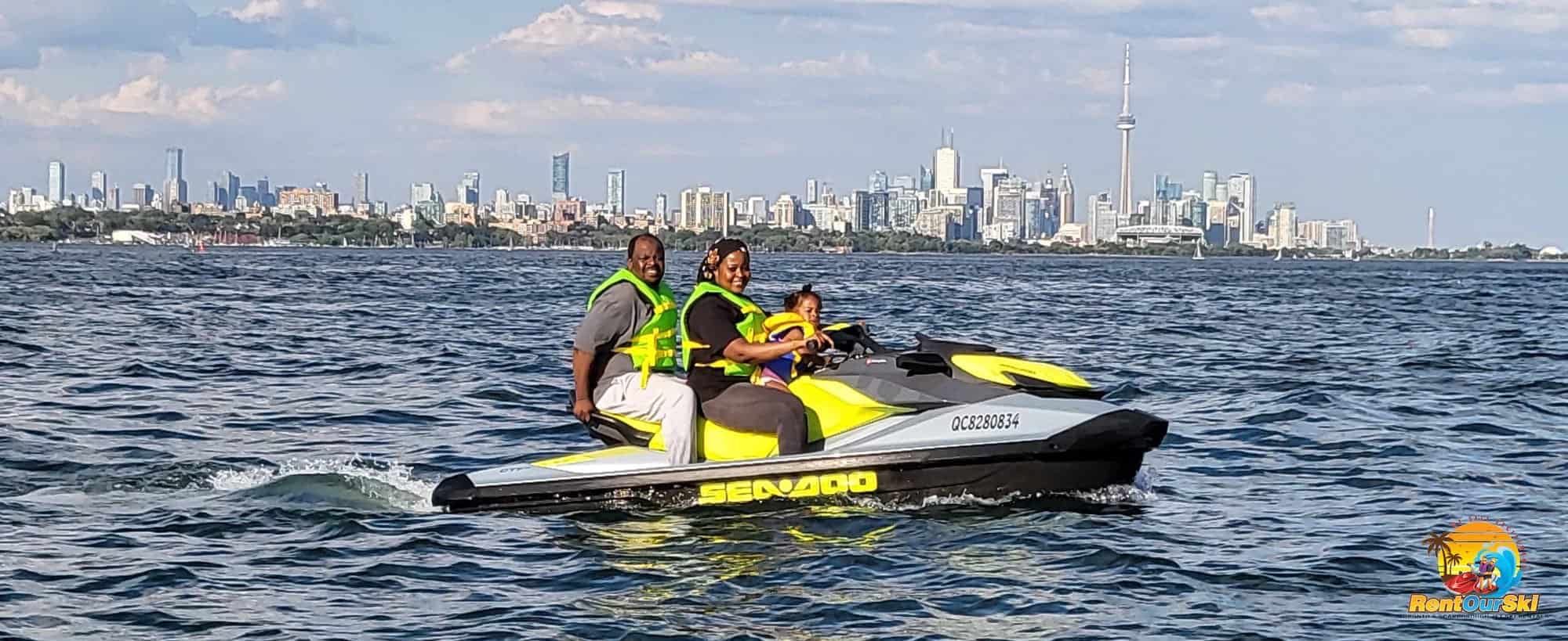 Family of three riding Neon Yellow rented Sea-Doo on Lake Ontario, with the Toronto Skyline in the background.